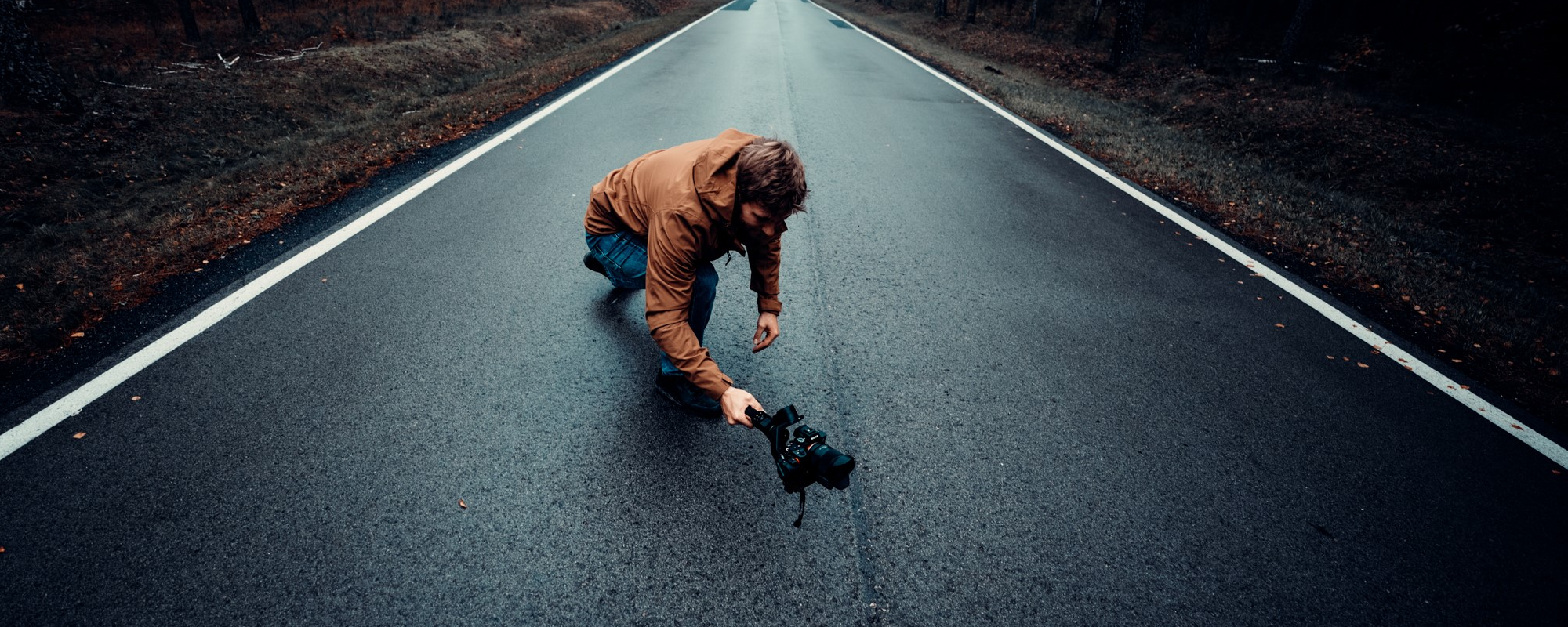 Zdjęcie - osoba na środku drogi, kucająca, trzymająca w ręku gimbala i filmująca coś z niskiej perspektywy